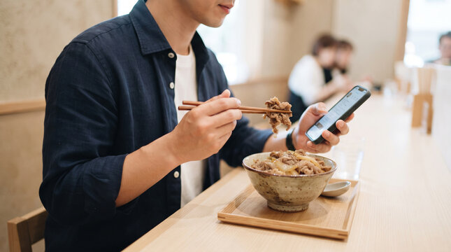 スマートフォンを操作しながら一人で食事をする男性