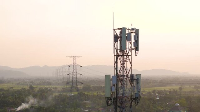 Aerial view of a telecommunications tower and power lines in a rural landscape during golden hour in Bayat, Central Java, Indonesia.