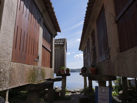 View of traditional stone horreos with wooden doors and potted plants overlooking the sea in Combarro, Pontevedra, Spain.