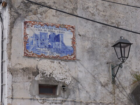 View of a blue and white tile mural depicting the historic Paco de Flor da Rosa castle on a weathered stone wall with a vintage street lamp in Portalegre, Portalegre District, Portugal.