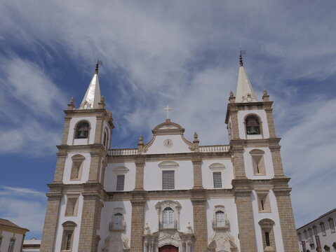 View of the facade of the historic Se de Portalegre cathedral with twin bell towers, white walls, and stone detailing under a blue sky in Portalegre, Portalegre District, Portugal.
