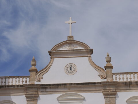 View of the white facade of the Se de Portalegre cathedral featuring a stone cross and a sundial under a blue sky in Portalegre, Portalegre District, Portugal.