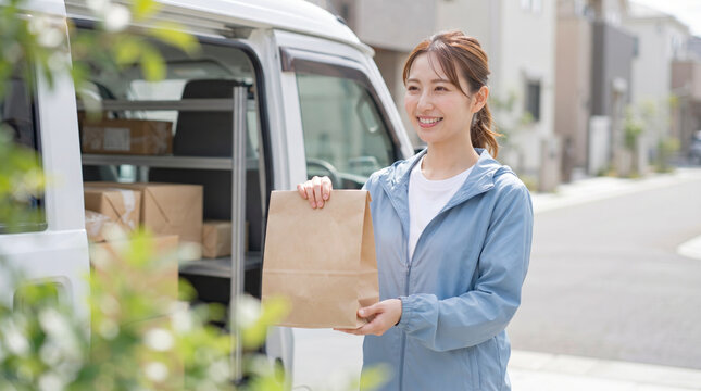 笑顔で荷物を手渡す配達員の女性と配送車
