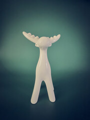 A single white reindeer figurine against a green background with generous copy space above. Minimalist vertical Christmas composition for seasonal greetings and festive advertising. © EvaMara