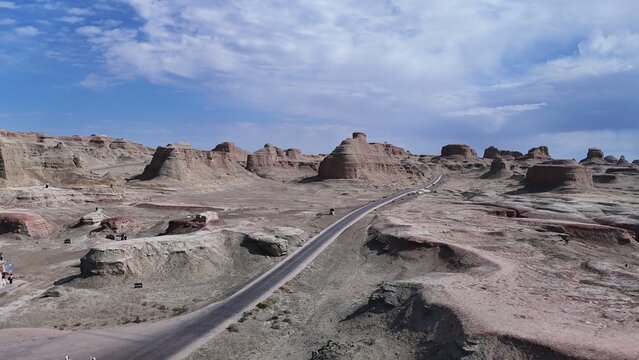 A road winding through the "Devil's City" in the Urho District of Karamay, Northern Xinjiang, China&mdash;a landscape of rocky desert terrain featuring strange formations resembling towers and animals.
