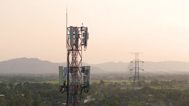 Aerial view of telecommunications tower standing in a rural landscape with distant mountains under a soft golden hour sky in Bayat, Central Java, Indonesia.