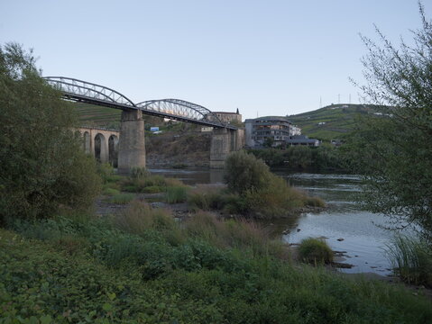 View of the metal truss bridge spanning the Douro River with terraced vineyards and buildings in the background in Peso da Regua, Vila Real District, Portugal.
