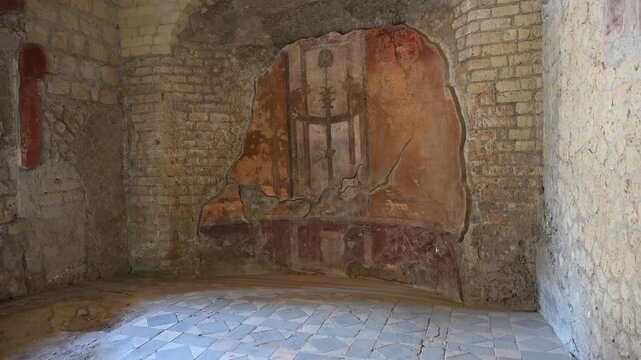 ERCOLANO, ITALY - SEPTEMBER 20, 2026: Ancient Roman wall fresco with red panels and geometric black and white tile floor inside a house at Herculaneum archaeological site.