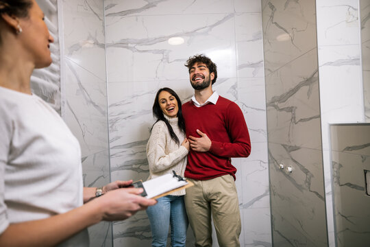 Happy couple inspecting new bathroom with real estate agent during tour