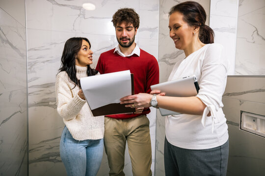 Realtor explaining terms on clipboard to young couple during apartment inspection