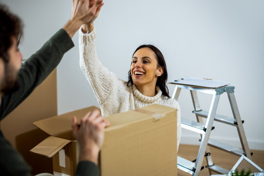 Excited couple giving high five while packing cardboard boxes in new home
