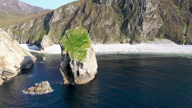 Aerial view of Glenlough Bay featuring a prominent sea stack, sandy beach, and steep cliffs along the rugged coastline of Ardara, County Donegal, Ireland.
