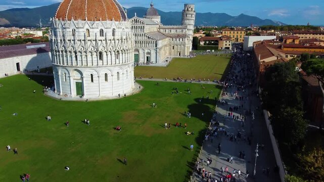 Aerial view of the Leaning Tower of Pisa and the surrounding historic Piazza dei Miracoli with tourists on the green lawns in Pisa, Toscana, Italy.