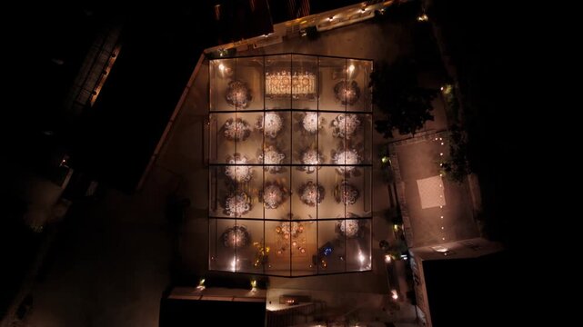 Aerial view of a wedding reception held inside an illuminated glass-walled tent at night with elegant table settings in Giao, Porto, Portugal.
