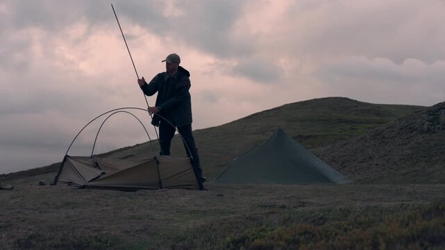 A man erecting a tent on a hill beside another while camping