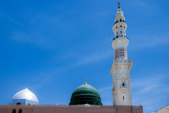 View of the iconic green dome and a tall white minaret of Al Masjid-e-Nabawi against a clear blue sky in Madinah, Al Madinah Province, Saudi Arabia.