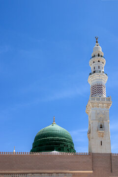 View of the iconic green dome and a tall white minaret of Al Masjid-e-Nabawi under a clear blue sky in Madinah, Al Madinah Province, Saudi Arabia.