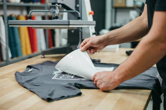 Person peeling transfer paper off a custom printed tshirt in a workshop