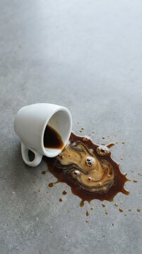 Spilled Coffee Cup on Gray Surface with Swirling Liquids