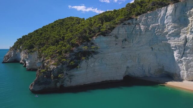 Vignanotica white cliff Beach Gargano Puglia Italy sea caves and canoe boat aerial drone rotation reveal of vertical limestone cliffs turquoise water wild coast travel 4k video
