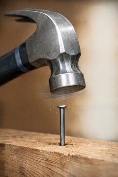 A hammer hits a nail on a wooden plank, with wood shavings around