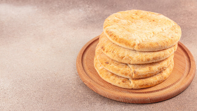Stack of round golden baked flatbreads with toasted surfaces arranged on a wooden serving board against a warm neutral background, top view food composition