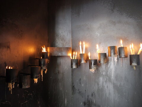 View of burning votive candles placed in metal holders against a dark, soot-stained wall in a church in Porto, Portugal.