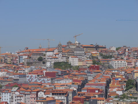 View of the historic cityscape of Porto with its iconic orange tiled rooftops, traditional architecture, and construction cranes under a clear blue sky in Porto, Porto District, Portugal.