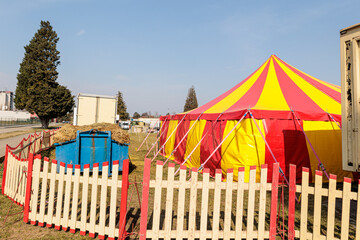 Red and Yellow Circus Tents Behind Picket Fence at Empty Outdoor Carnival Field © Olga
