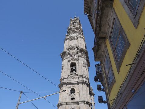 View of Clerigos Tower rising against a clear blue sky, with a yellow historic building facade visible on the right in Porto, Porto District, Portugal.