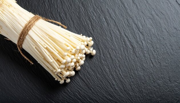Bundle of Enoki Mushrooms Tied With Twine on Dark Slate Surface
