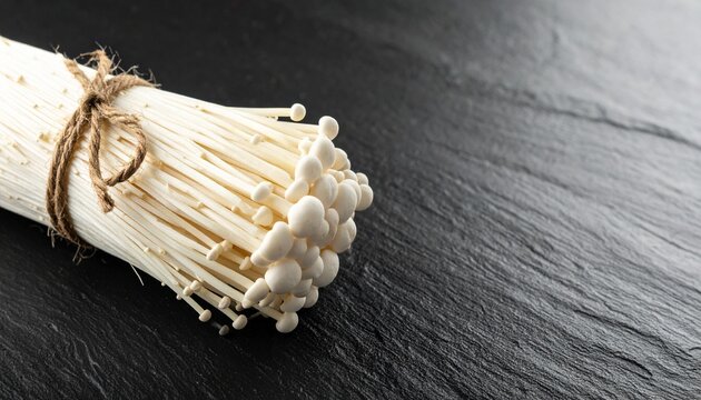 Bundle of Enoki Mushrooms Tied with Twine on a Dark Slate Surface