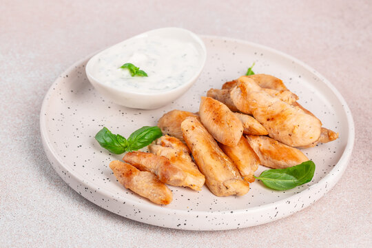 Breaded golden chicken strips arranged on a speckled ceramic plate with creamy dipping sauce and fresh basil leaves, photographed from above