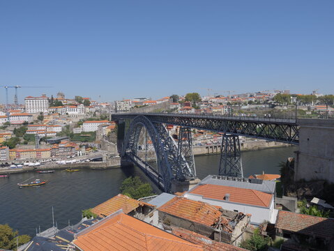 View of the iconic Dom Luis I Bridge spanning the Douro River with historic buildings and terracotta rooftops in the background in Porto, Porto District, Portugal.