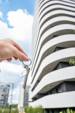 Vertical Close up of Hand Holding House Keys with Keychain against Modern Apartment Skyscraper