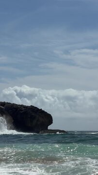 Low angle coastal view with breaking waves, foamy surf, and rugged rocky headland, wispy sky with cirrus and cumulus clouds, sparkling reflections on wet sand