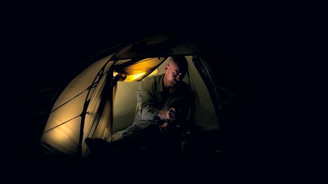 A man cooking food inside a tent at night 