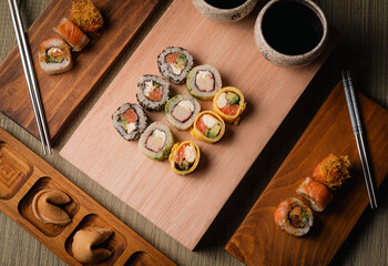 Variedad de piezas de sushi en tablas de madera con salsa de soja palillos y galletas de la fortuna vista cenital © Sonne Studio