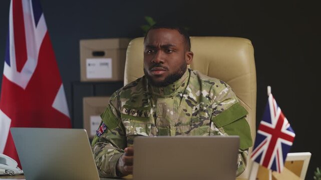 Black U.K. intelligence officer works on laptops in military hub, defense policy