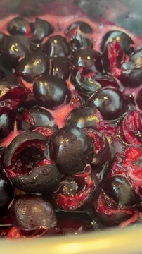 Macro close view of halved dark cherries in shallow cookware releasing glossy red purple juices with bubbles and foam under warm specular highlights for food styling