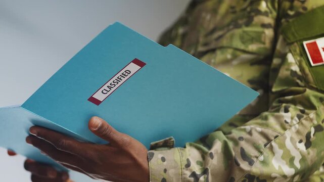 Black Canadian army officer reads confidential reports from classified folder