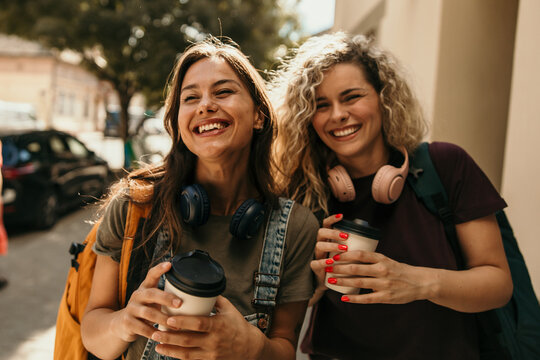 Two young women laughing and walking with coffee cups