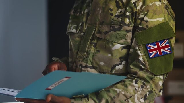 Black U.K. army officer reviews confidential reports from classified folder