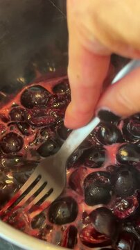 Hand stirring simmering cherries in a pan