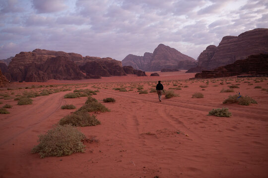 Lonely traveler walking in the red sand valley of Wadi Rum desert. Spiritual journey, exploration and life path concept in Jordan.