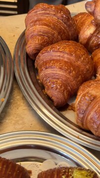 Closeup bakery pastry display showing plated croissants and pistachio topped pastries on mirrored metal platters with warm ambient highlights