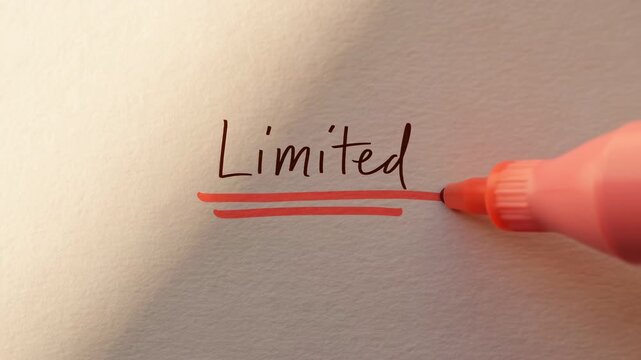 Pink marker draws two bold underline strokes beneath handwritten word Limited on textured cream paper, moving left to right in close-up under warm soft light with minimal composition