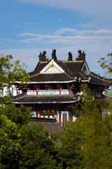 Fototapeta premium Traditional Chinese Pavilion with Curved Roofs and Green Trees Against Blue Sky