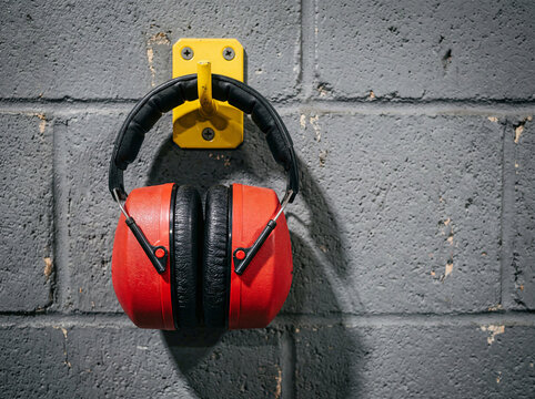 Red protective ear defenders hanging on wall hook for workplace hearing safety