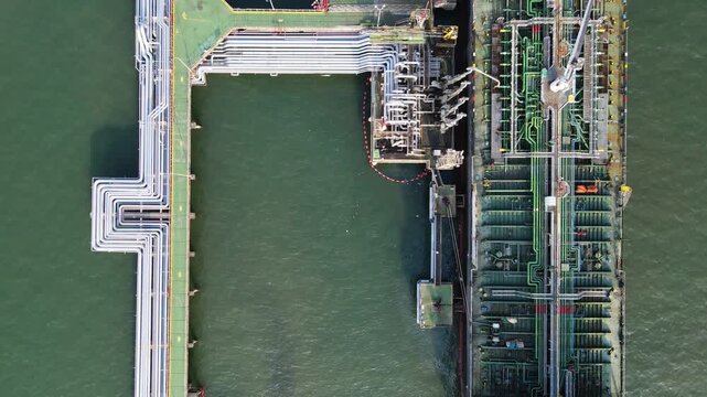Aerial view of an oil tanker docked at an industrial terminal with complex pipeline infrastructure in the sea near Cilacap Regency, Central Java, Indonesia.
